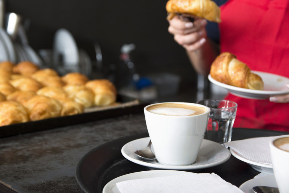 coffee-cup-front-waitress-placing-croissant-plate-1000x667 - El pintoresco bar al que iba el Che Guevara en el corazón de Palermo en la Ciudad de Buenos Aires con ricas comidas típicas argentinas