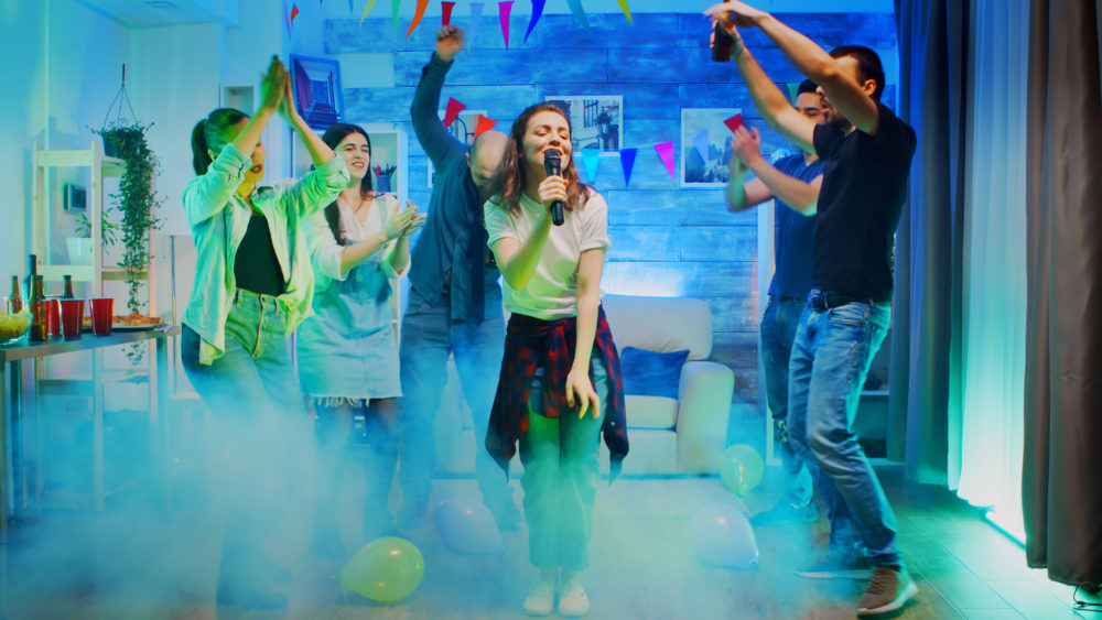 cheerful-young-woman-singing-her-friends-party-room-with-neon-lights-smoke-1000x563 - 6 karaokes en Madrid para divertirte con tus amigos